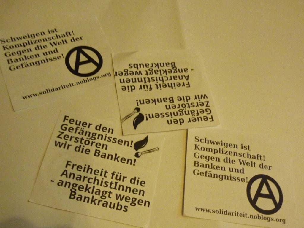 Flyer avec l'allumette dit: "Feu aux prisons! Détruisons les banques! Liberté pour les anarchistes accusées de braquage de banque" / Le flyer avec le (A): "Le silence (face aux flics, NdT) signifie complicité ! Contre le monde des banques et des prisons"